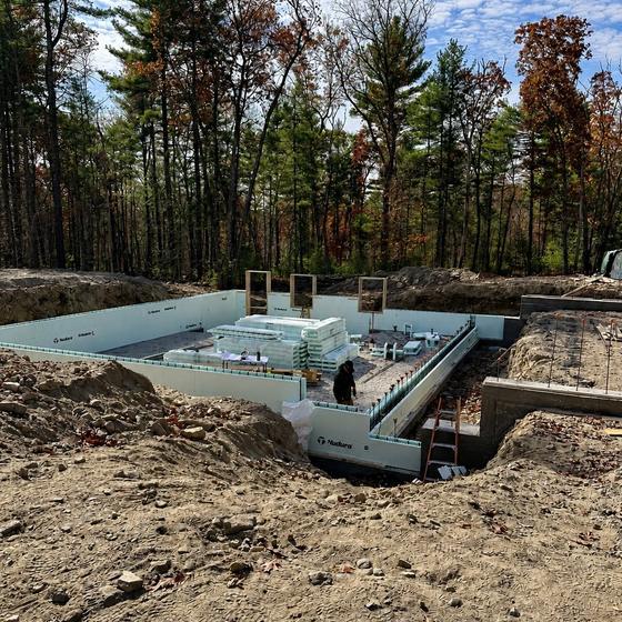 Nudura insulated concrete form foundation walls poured on a wooded lot, with a worker inside the footprint